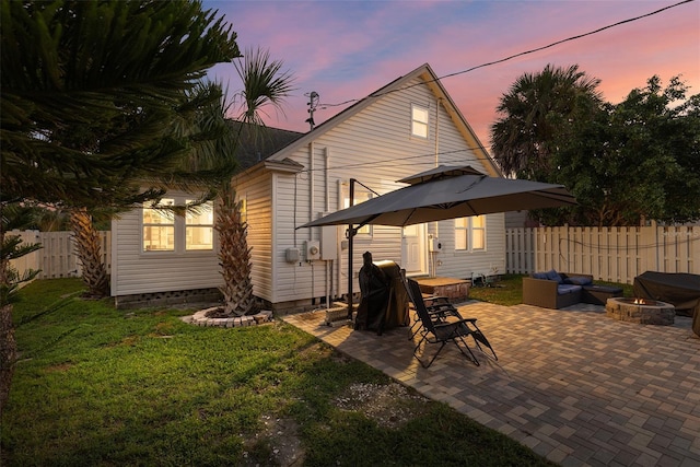 back of house at dusk featuring a yard, an outdoor living space with a fire pit, a patio area, and fence