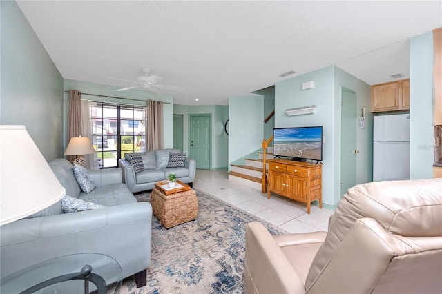 living room with light tile patterned floors, ceiling fan, visible vents, and stairs