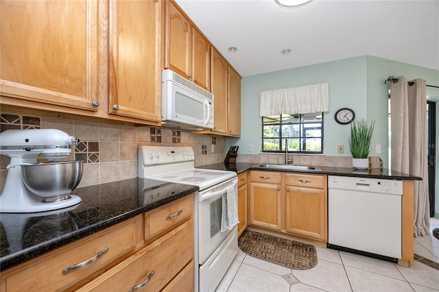 kitchen featuring light tile patterned floors, tasteful backsplash, a sink, dark stone counters, and white appliances