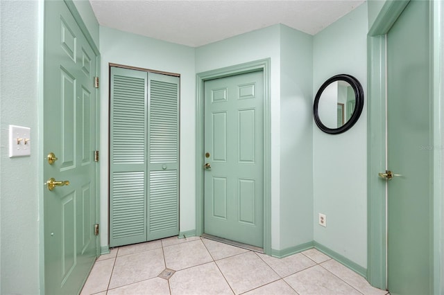 foyer with light tile patterned floors, a textured ceiling, and baseboards