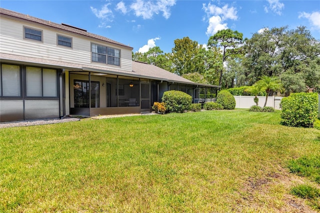 rear view of house featuring a lawn, fence, and a sunroom