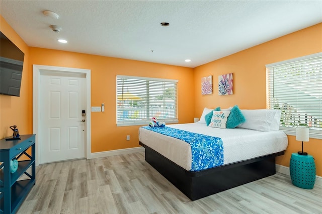 bedroom with light wood-style floors, baseboards, and a textured ceiling