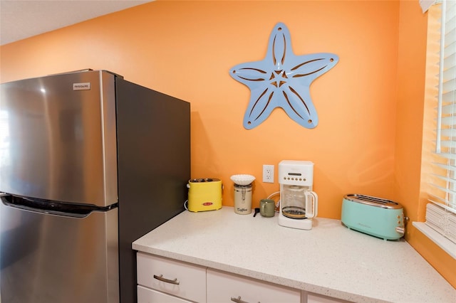 kitchen featuring light stone counters, white cabinets, and stainless steel refrigerator