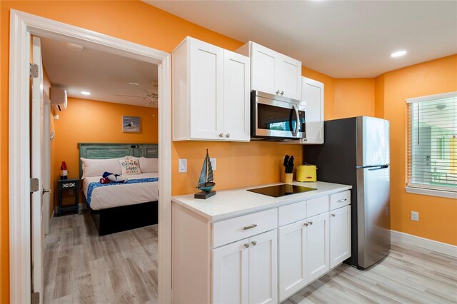 kitchen featuring white cabinets, light wood-type flooring, a wall unit AC, and stainless steel appliances