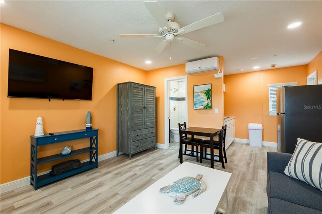 living room featuring light hardwood / wood-style floors, ceiling fan, and an AC wall unit