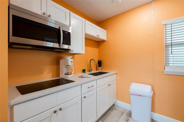 kitchen featuring black electric stovetop, stainless steel microwave, a sink, and white cabinetry