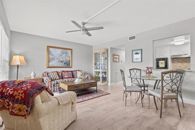 living room featuring ceiling fan, light hardwood / wood-style floors, and a textured ceiling