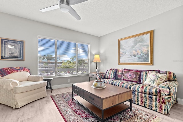 living room featuring ceiling fan, light hardwood / wood-style flooring, and a textured ceiling