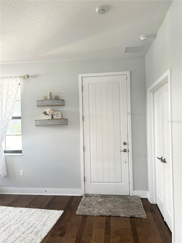 doorway to outside with dark wood-style floors, a textured ceiling, and baseboards