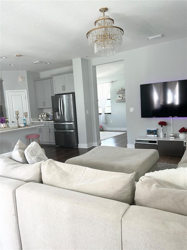 living room featuring dark wood-style floors, a textured ceiling, and an inviting chandelier