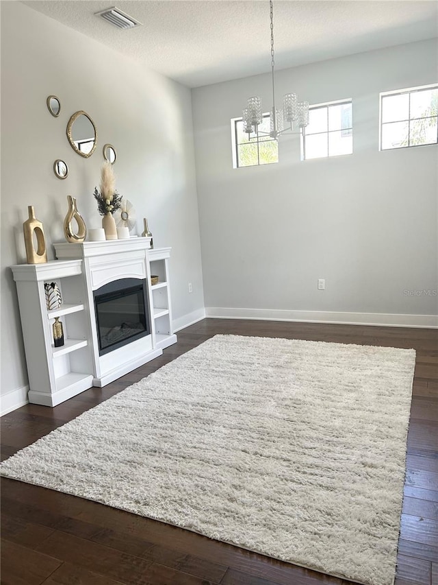 unfurnished living room with a textured ceiling, dark wood-style flooring, visible vents, baseboards, and a glass covered fireplace