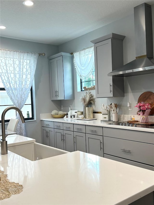 kitchen featuring a textured ceiling, black electric stovetop, gray cabinetry, light countertops, and wall chimney range hood