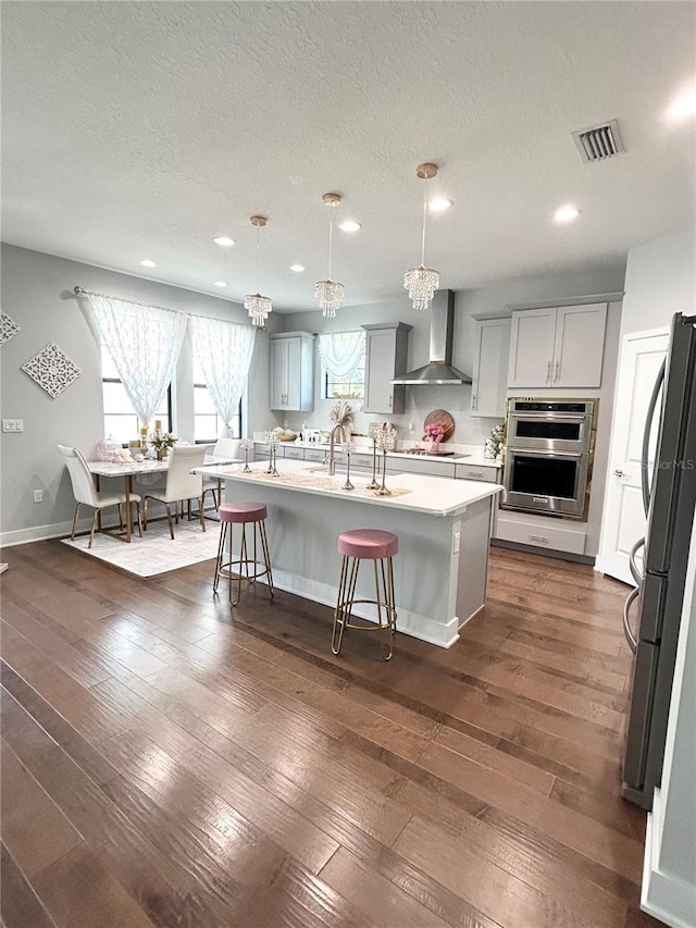 kitchen featuring wall chimney range hood, visible vents, dark wood finished floors, and stovetop