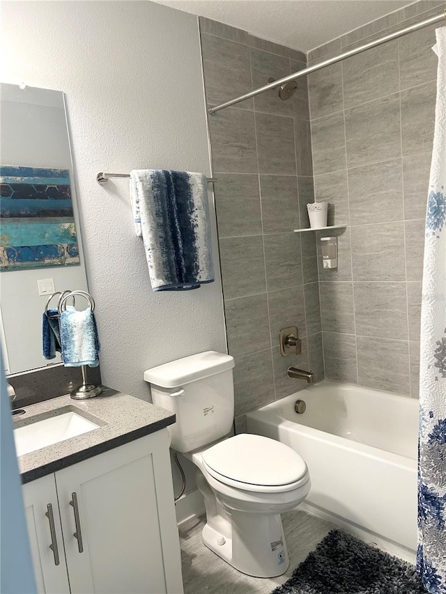 full bathroom featuring a textured wall, shower / tub combo with curtain, vanity, and toilet