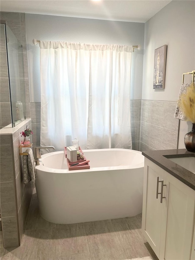 full bath featuring a freestanding tub, a tile shower, tile walls, and vanity