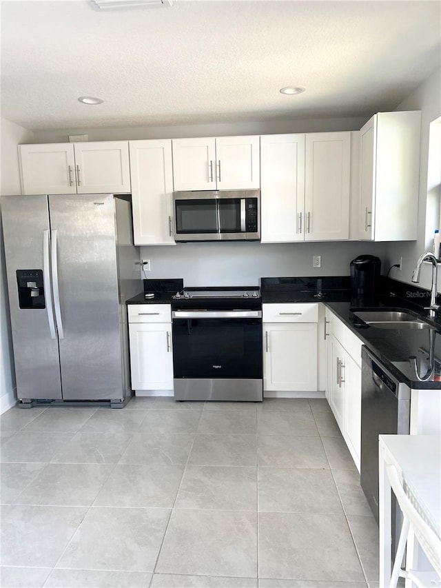 kitchen featuring light tile patterned flooring, a sink, white cabinetry, appliances with stainless steel finishes, and dark countertops