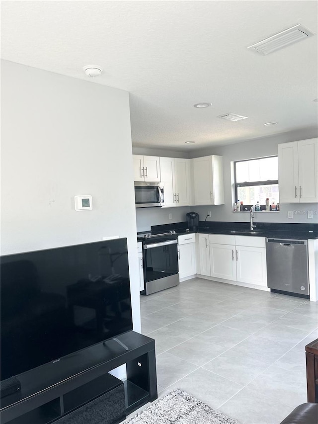 kitchen featuring visible vents, white cabinets, dark countertops, appliances with stainless steel finishes, and a sink