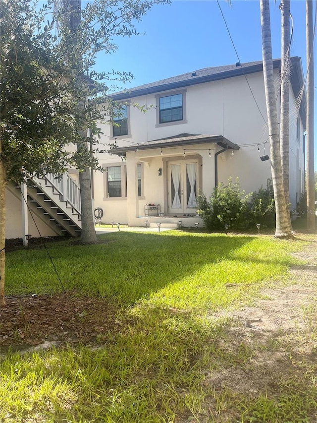 back of house featuring stairway, a lawn, and stucco siding