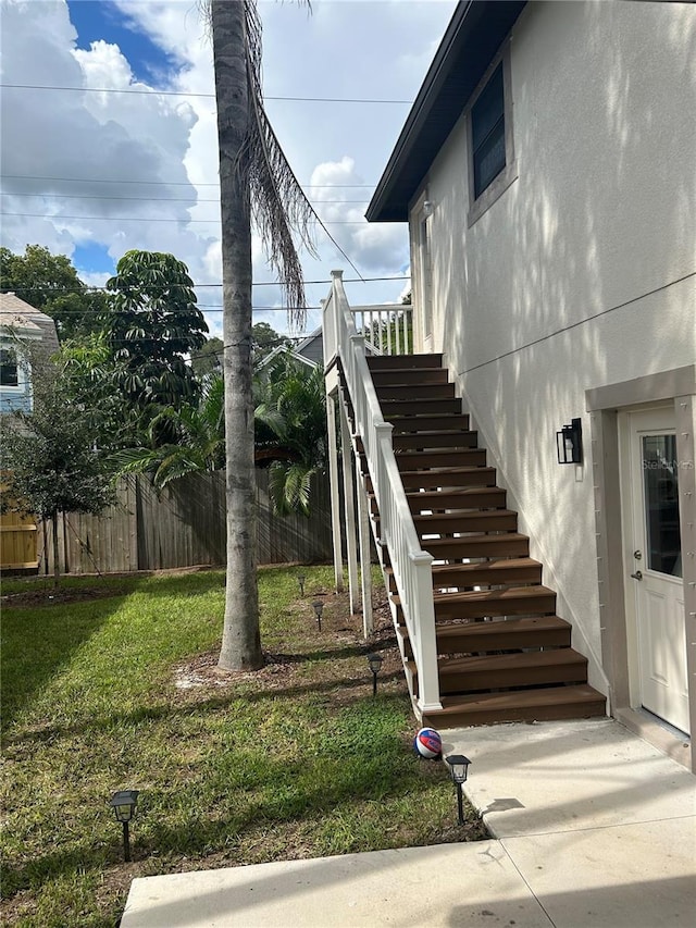 view of property exterior with stairs, a yard, fence, and stucco siding