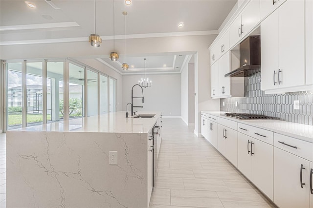 kitchen featuring a kitchen island with sink, sink, white cabinets, and decorative light fixtures