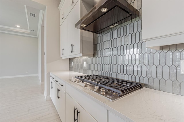 kitchen featuring white cabinets, backsplash, stainless steel gas stovetop, and wall chimney range hood