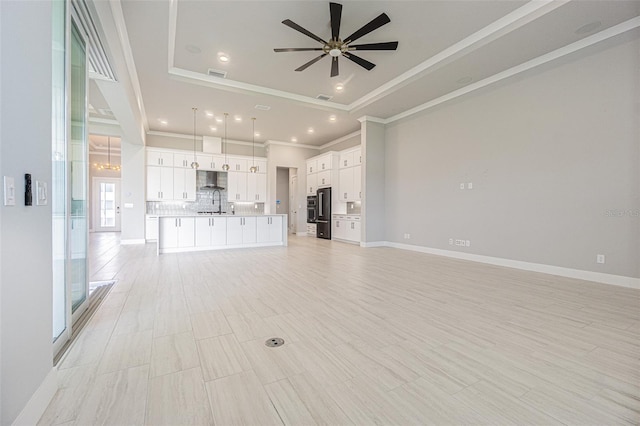 unfurnished living room featuring a tray ceiling, ceiling fan, sink, and ornamental molding