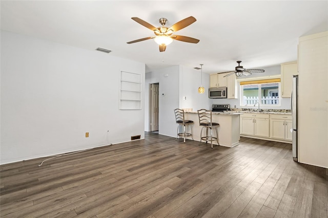 kitchen featuring appliances with stainless steel finishes, dark wood-type flooring, a peninsula, a kitchen bar, and a sink