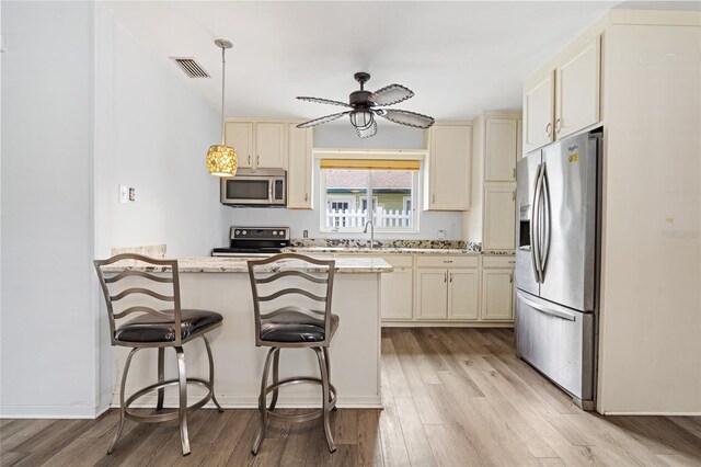 kitchen featuring stainless steel appliances, light hardwood / wood-style flooring, a kitchen bar, light stone countertops, and ceiling fan