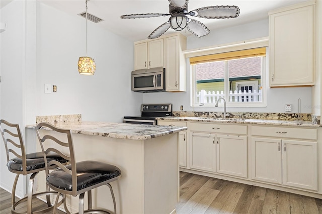 kitchen featuring sink, light wood-type flooring, electric stove, ceiling fan, and hanging light fixtures