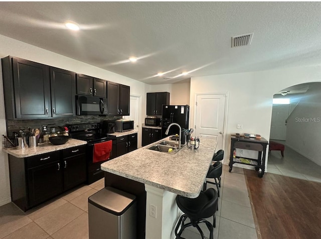 kitchen with decorative backsplash, a kitchen breakfast bar, a kitchen island with sink, sink, and black appliances