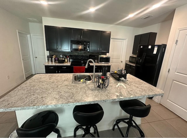 kitchen featuring light tile patterned flooring, backsplash, a kitchen breakfast bar, an island with sink, and black appliances