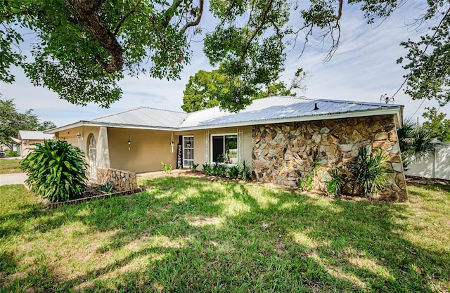 single story home with stone siding, metal roof, and a front yard