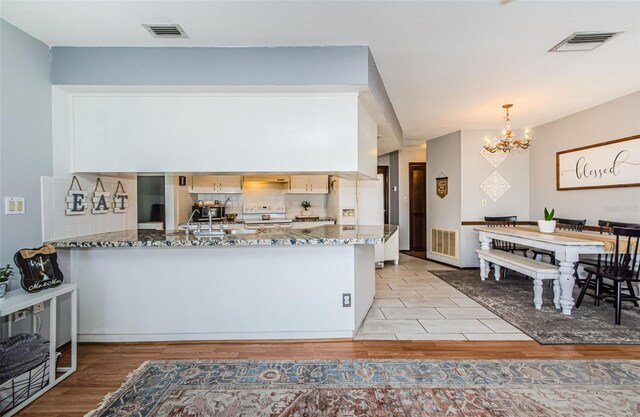 kitchen with an inviting chandelier, white appliances, light hardwood / wood-style flooring, pendant lighting, and light stone counters