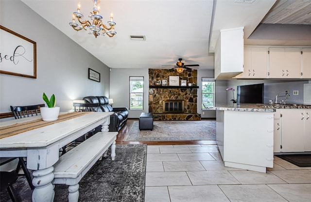 interior space featuring ceiling fan with notable chandelier, light tile patterned floors, a fireplace, and white cabinetry