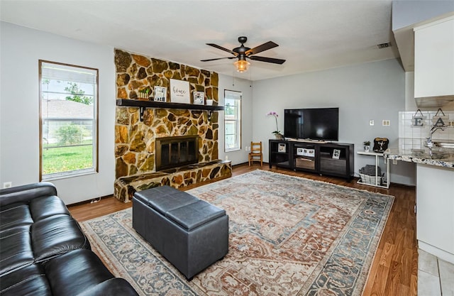 living area with a ceiling fan, visible vents, a stone fireplace, and wood finished floors