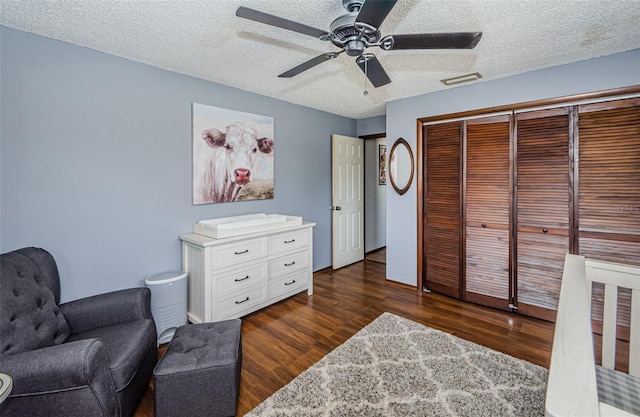 sitting room with a ceiling fan, dark wood-style flooring, visible vents, and a textured ceiling