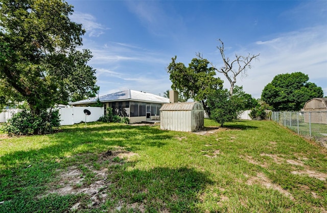 view of yard featuring a sunroom, a fenced backyard, and a storage unit