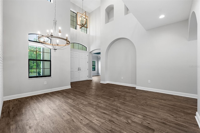 unfurnished living room featuring a high ceiling, a chandelier, and dark hardwood / wood-style flooring