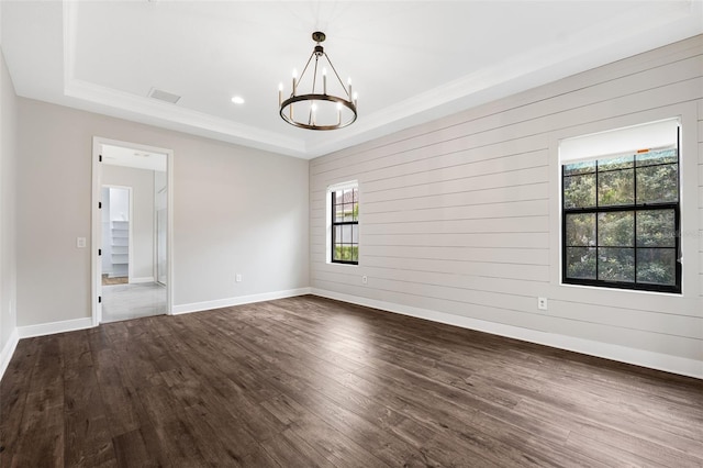 spare room with dark wood-type flooring, a healthy amount of sunlight, a raised ceiling, and an inviting chandelier