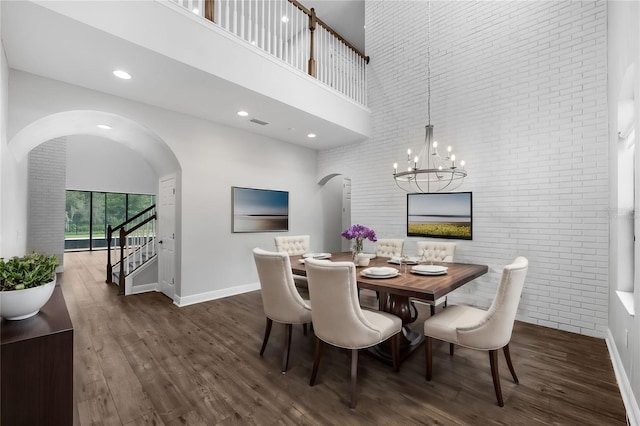 dining space featuring a high ceiling, dark hardwood / wood-style floors, brick wall, and a notable chandelier