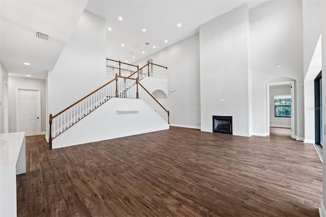 unfurnished living room featuring dark wood-type flooring, a high ceiling, and a large fireplace