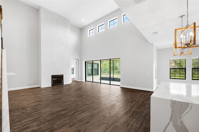 unfurnished living room featuring a towering ceiling, a large fireplace, dark hardwood / wood-style floors, and a chandelier