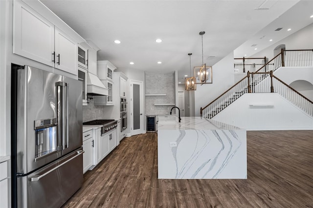 kitchen featuring white cabinetry, appliances with stainless steel finishes, an island with sink, and light stone countertops