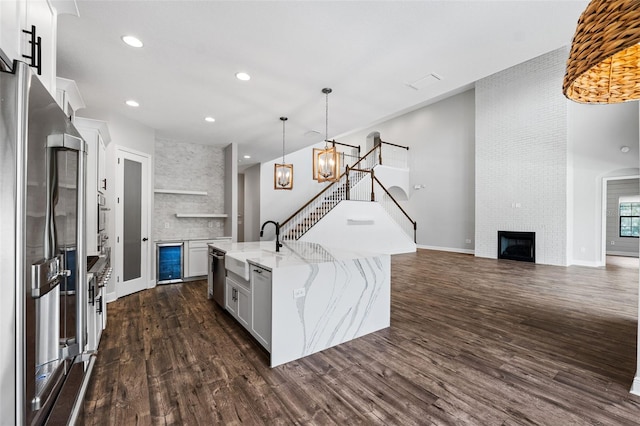 kitchen featuring dark wood-type flooring, white cabinets, an island with sink, appliances with stainless steel finishes, and decorative light fixtures