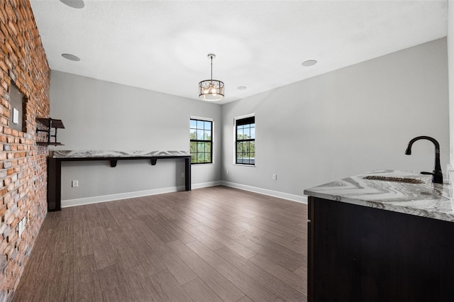 unfurnished living room with dark hardwood / wood-style floors, brick wall, sink, and a chandelier