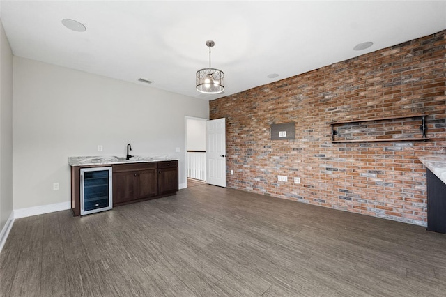 bar with brick wall, wine cooler, decorative light fixtures, dark brown cabinets, and dark hardwood / wood-style flooring