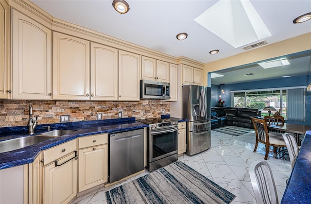 kitchen with a skylight, stainless steel appliances, sink, light tile patterned flooring, and decorative backsplash