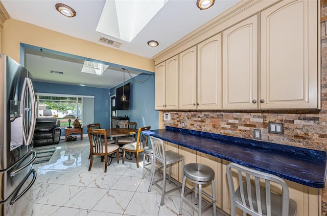 kitchen featuring stainless steel fridge, a skylight, cream cabinets, hanging light fixtures, and a breakfast bar