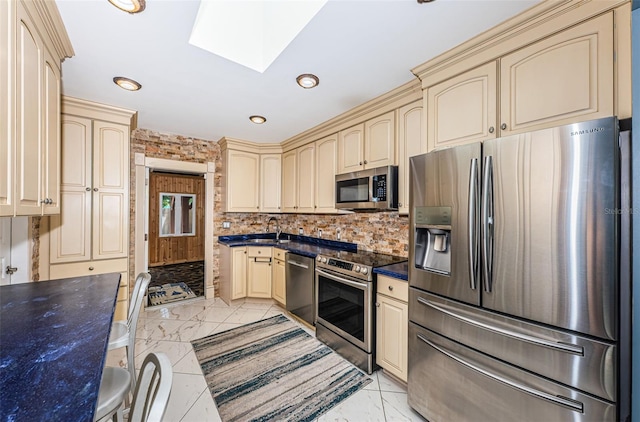 kitchen with cream cabinetry, a skylight, light tile patterned floors, decorative backsplash, and appliances with stainless steel finishes