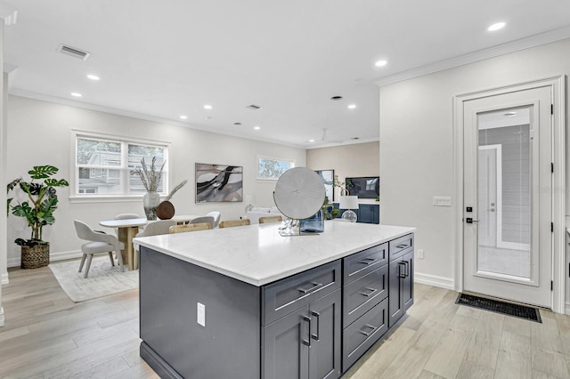 kitchen featuring ornamental molding, light wood-type flooring, visible vents, and a center island